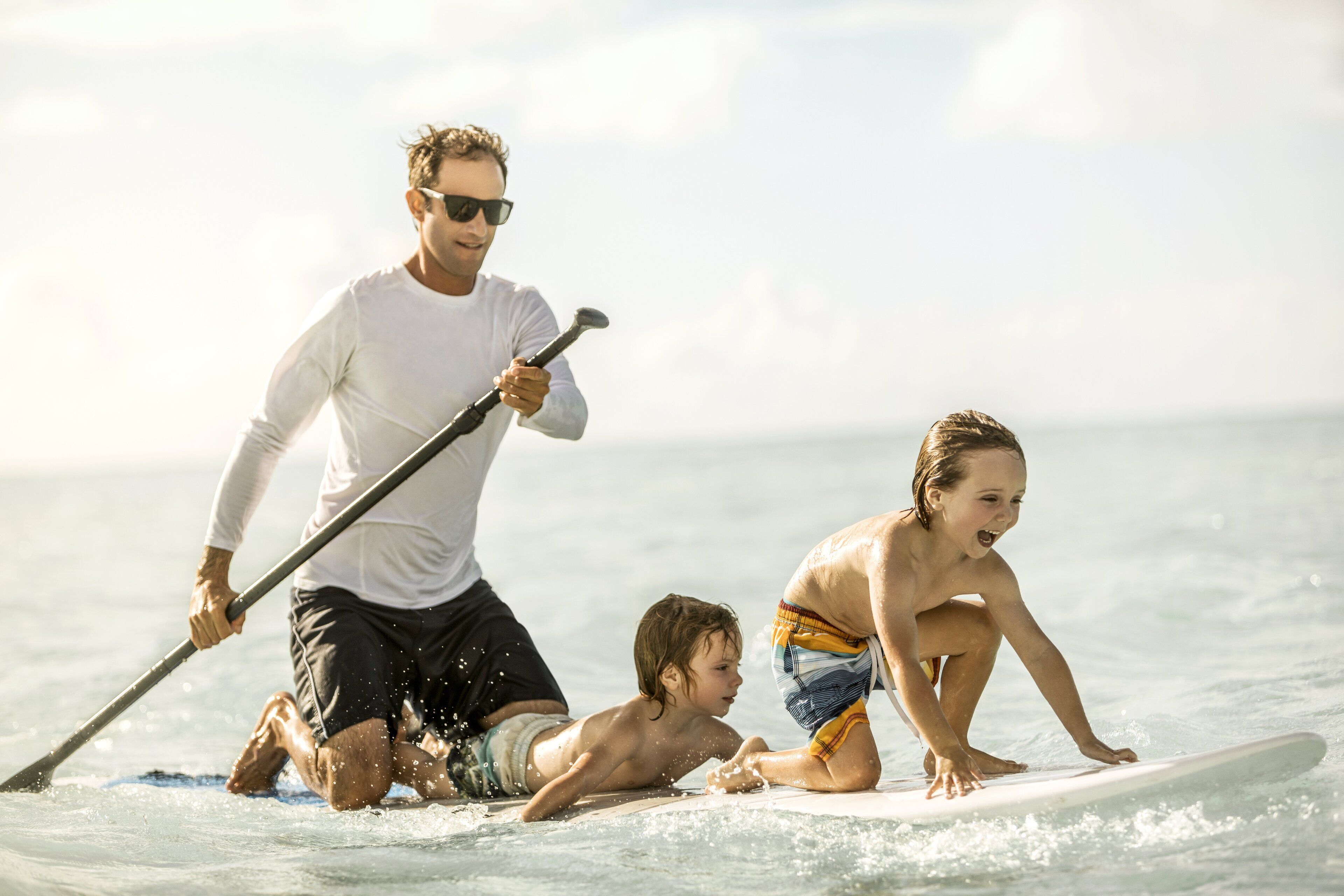 A man and two children paddleboarding on a calm sea.