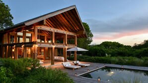 Une maison moderne dotée d’une grande terrasse, d’une piscine et d’un espace extérieur aménagé et abrité.