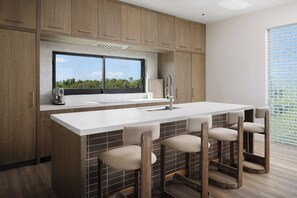 A modern kitchen with a large island, bar stools, and a window with a view of greenery.