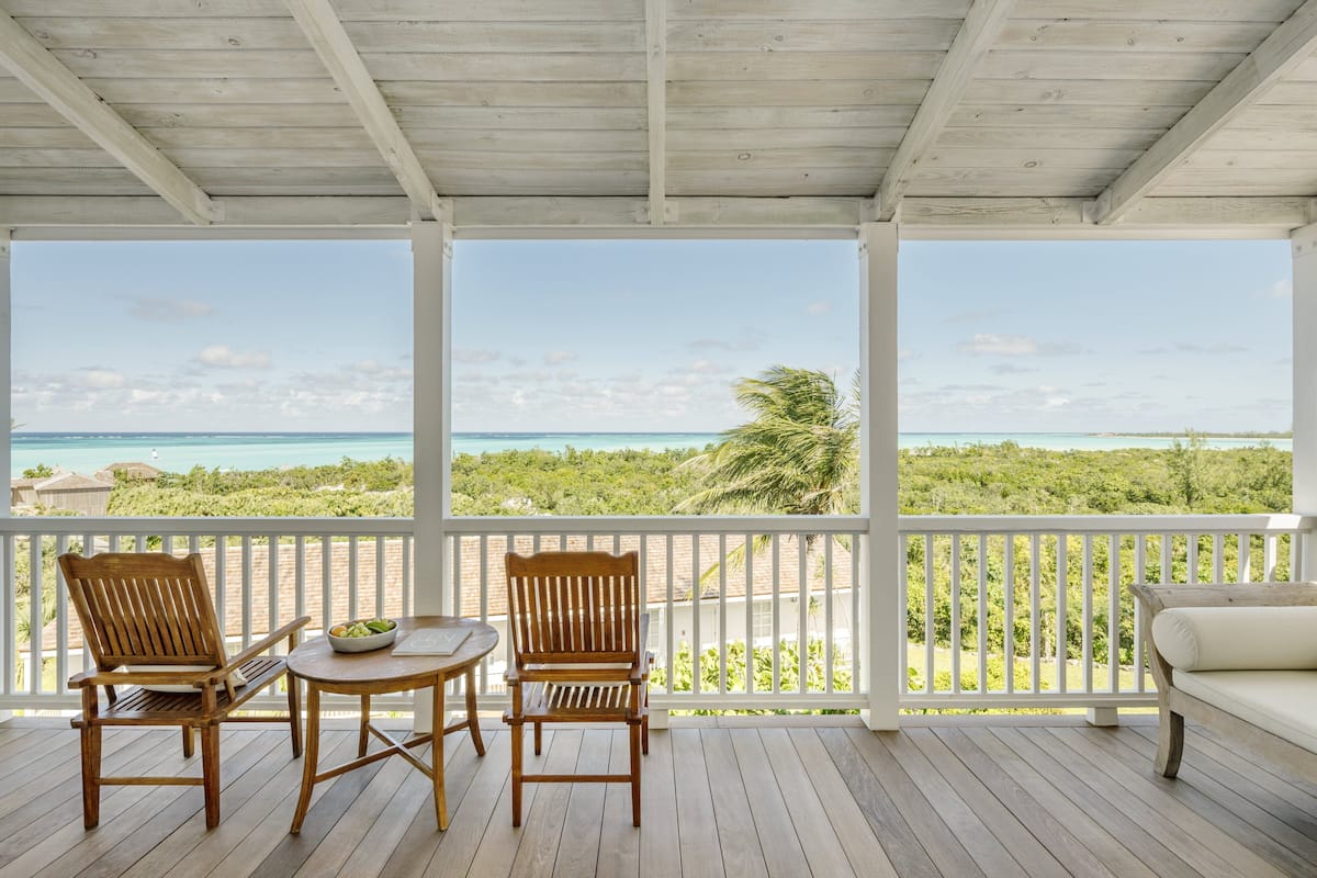 A wooden deck with two wooden chairs and a small table, overlooking a beach and ocean.