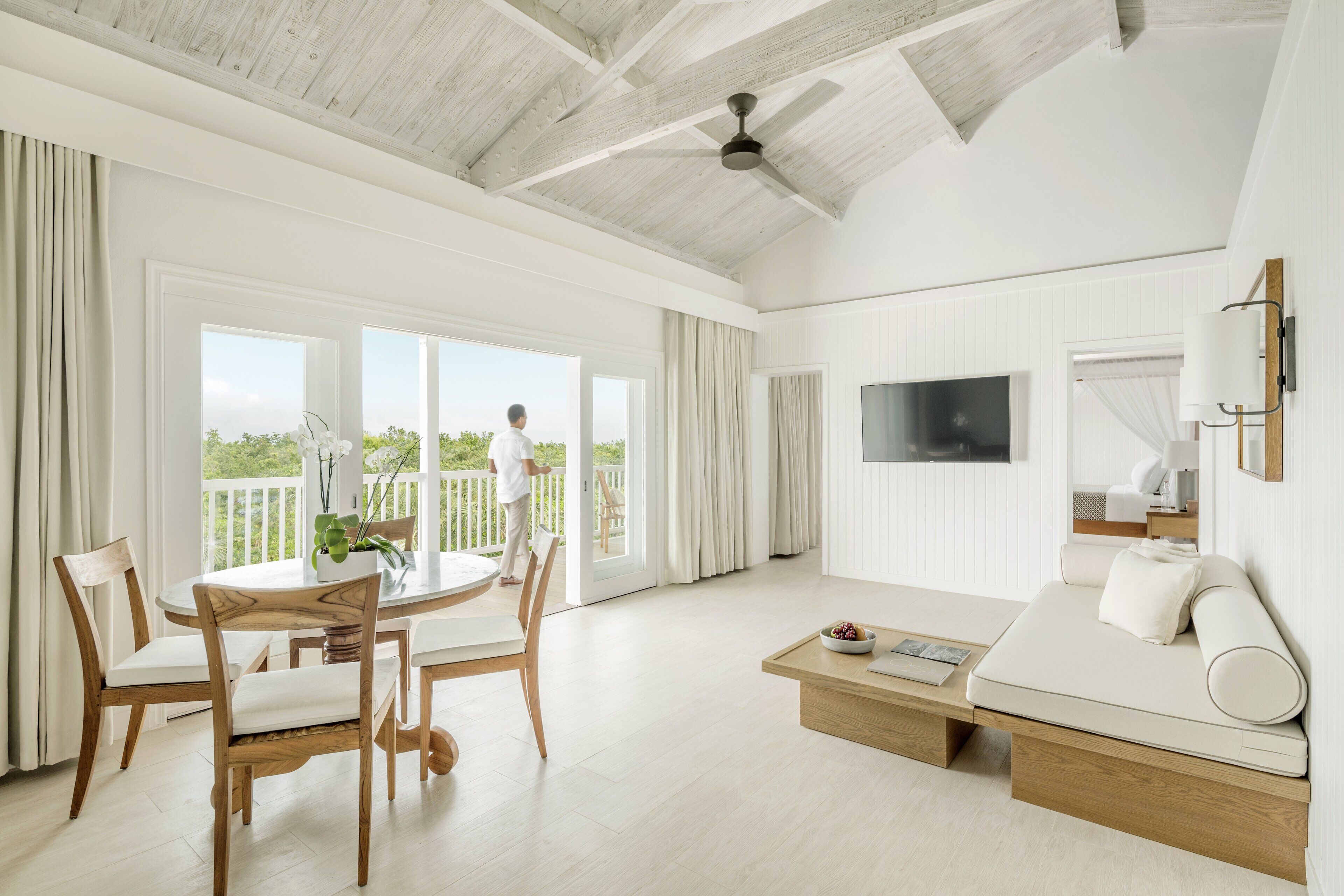 A spacious living room with a large window, a flat-screen TV, a sofa, and a dining area with wooden chairs and a table.
