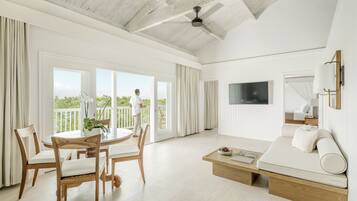 A spacious living room with a large window, a flat-screen TV, a sofa, and a dining area with wooden chairs and a table.