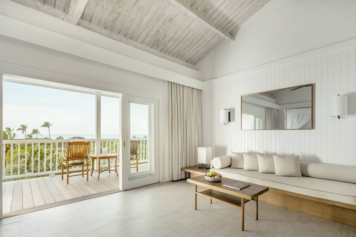 A modern room with a wooden ceiling, a balcony with a view, a sofa, a table, and a mirror on the wall.