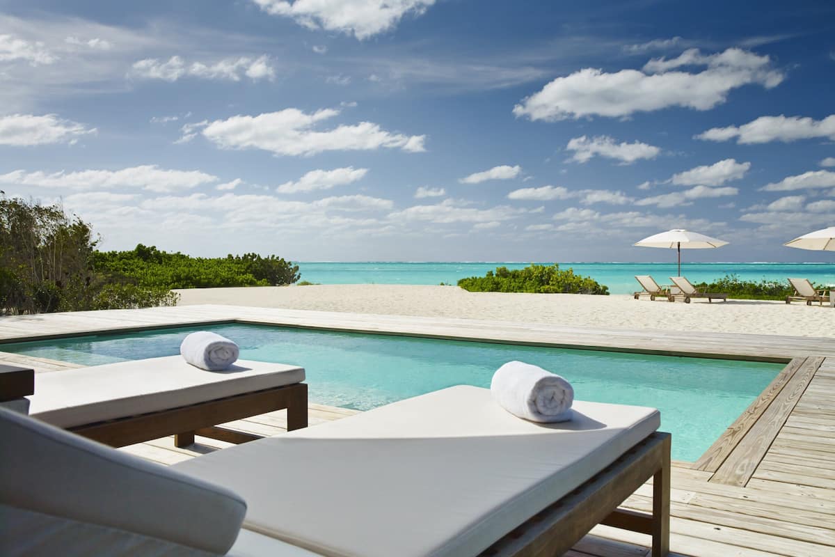 A poolside area with lounge chairs and umbrellas, overlooking a beach and ocean.