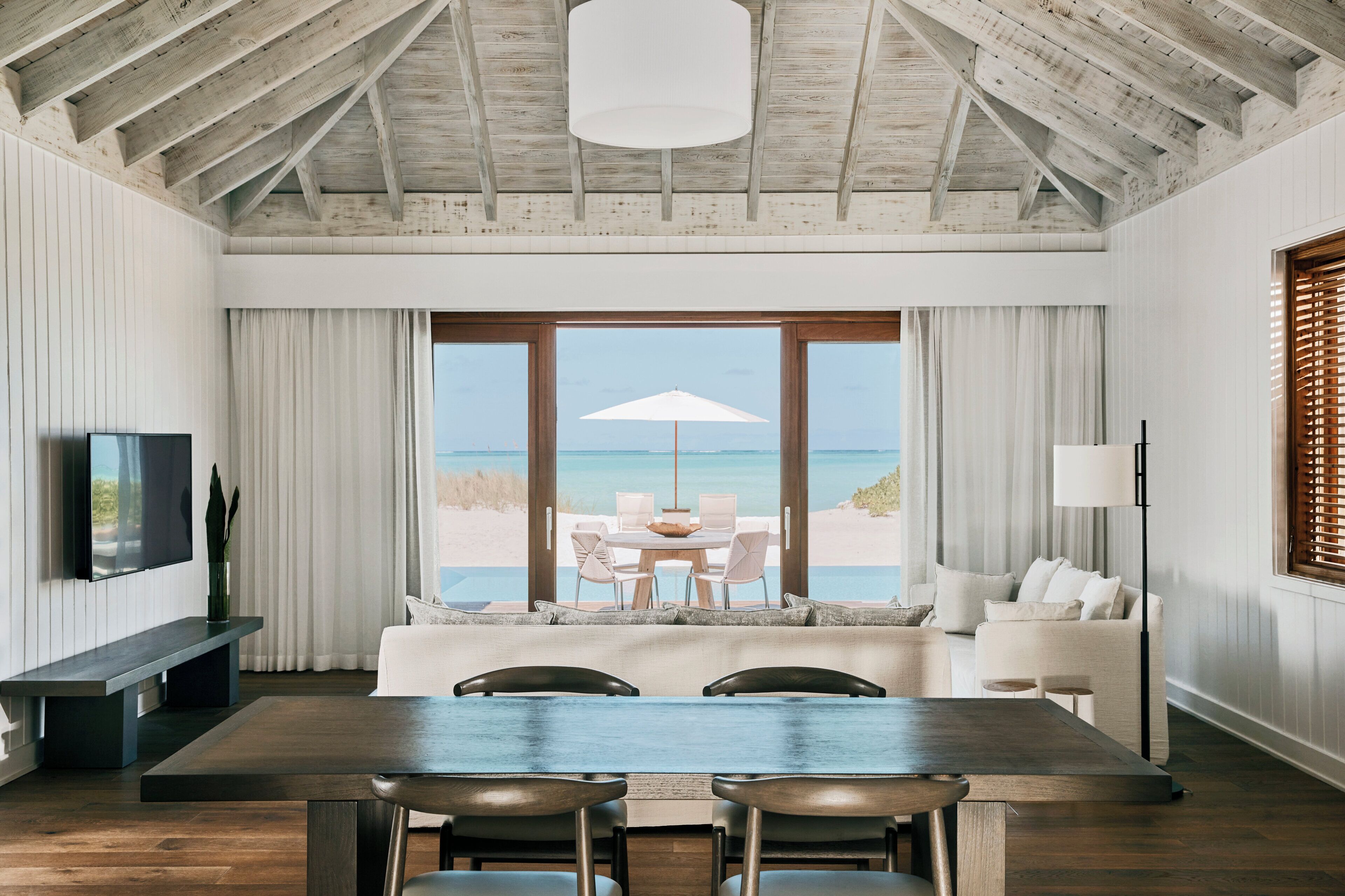 Un interior moderno con comedor, sofá y un amplio ventanal con vista a la playa.