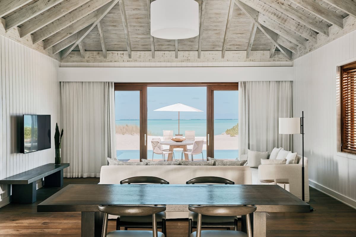 A modern interior with a wooden ceiling, a dining area with a view of the beach, and a seating area with a view of the ocean.