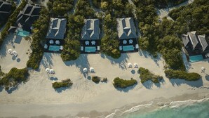 Vue aérienne d’un complexe hôtelier de bord de mer, composé de plusieurs bungalows, chacun doté d’une piscine privée et entouré d’une végétation luxuriante.