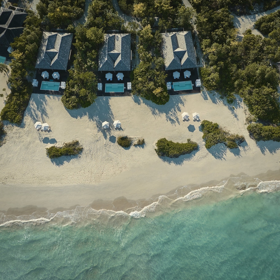 An aerial view of a beach resort with multiple bungalow-style accommodations, each with a private pool and surrounded by lush greenery.