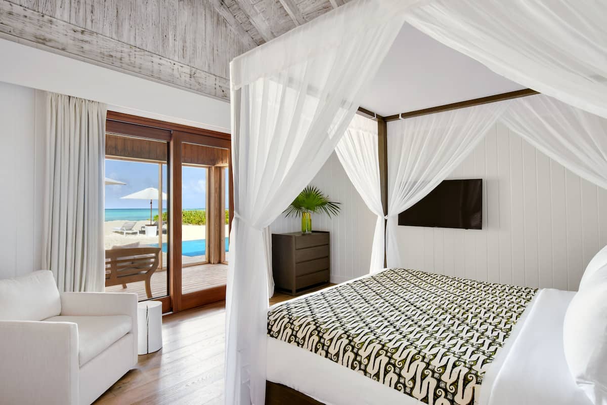 A bedroom with a bed, a nightstand, a TV, and a view of the beach.