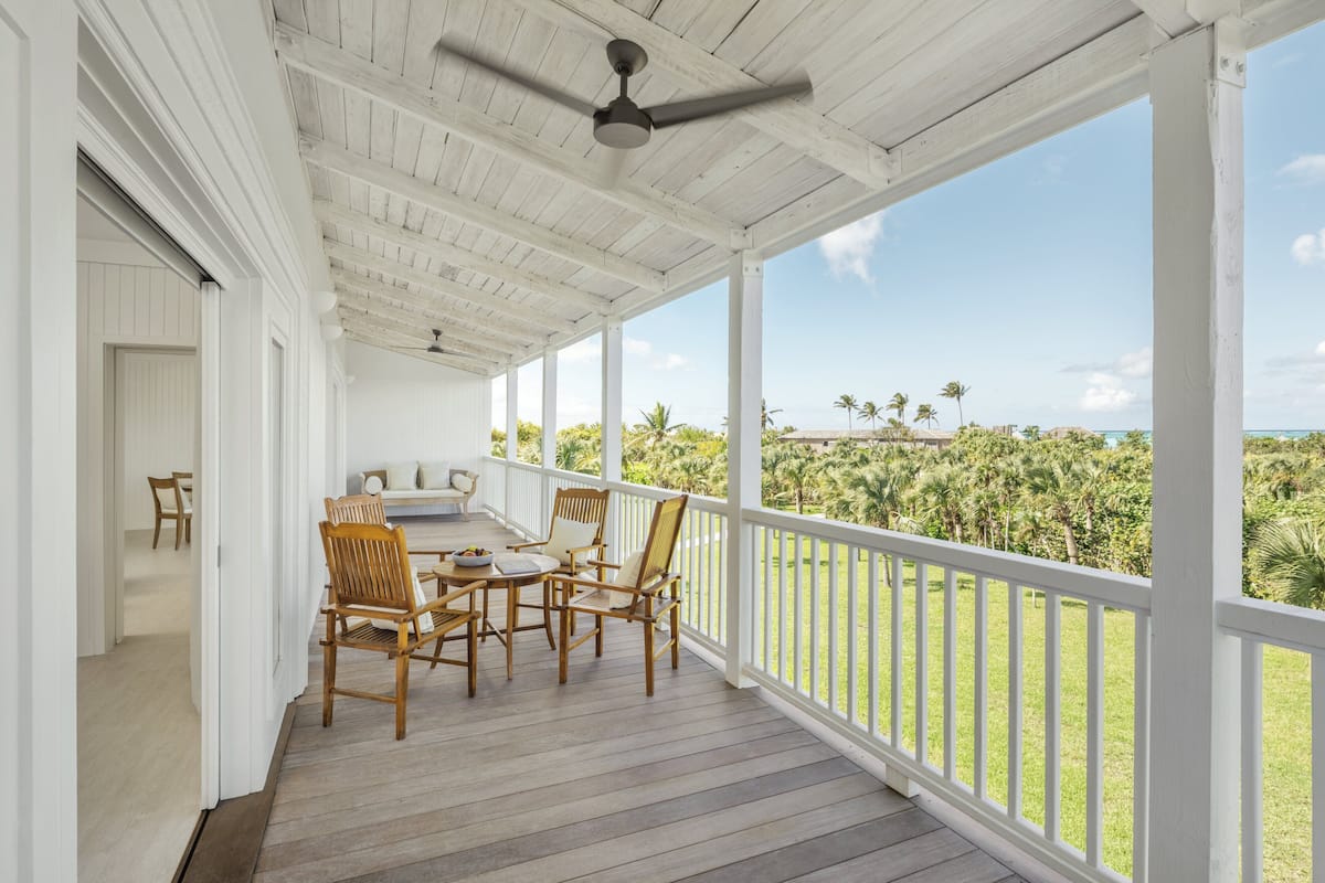 A covered porch with a table and chairs, overlooking a tropical landscape.