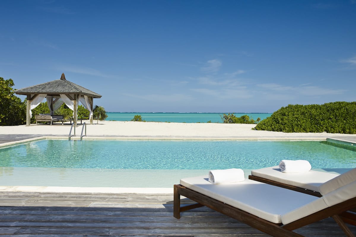 A pool with lounge chairs, a gazebo, and a view of the ocean.