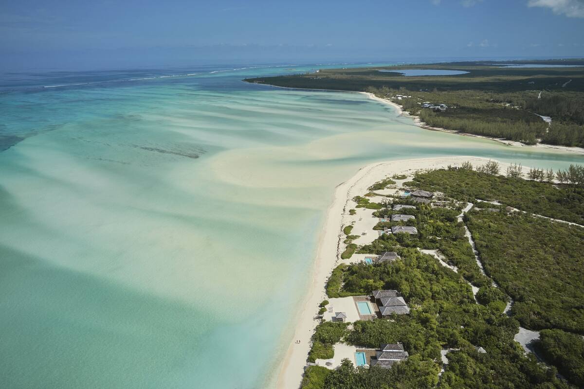 An aerial view of a coastal resort with clear turquoise waters, sandy beaches, and lush greenery.