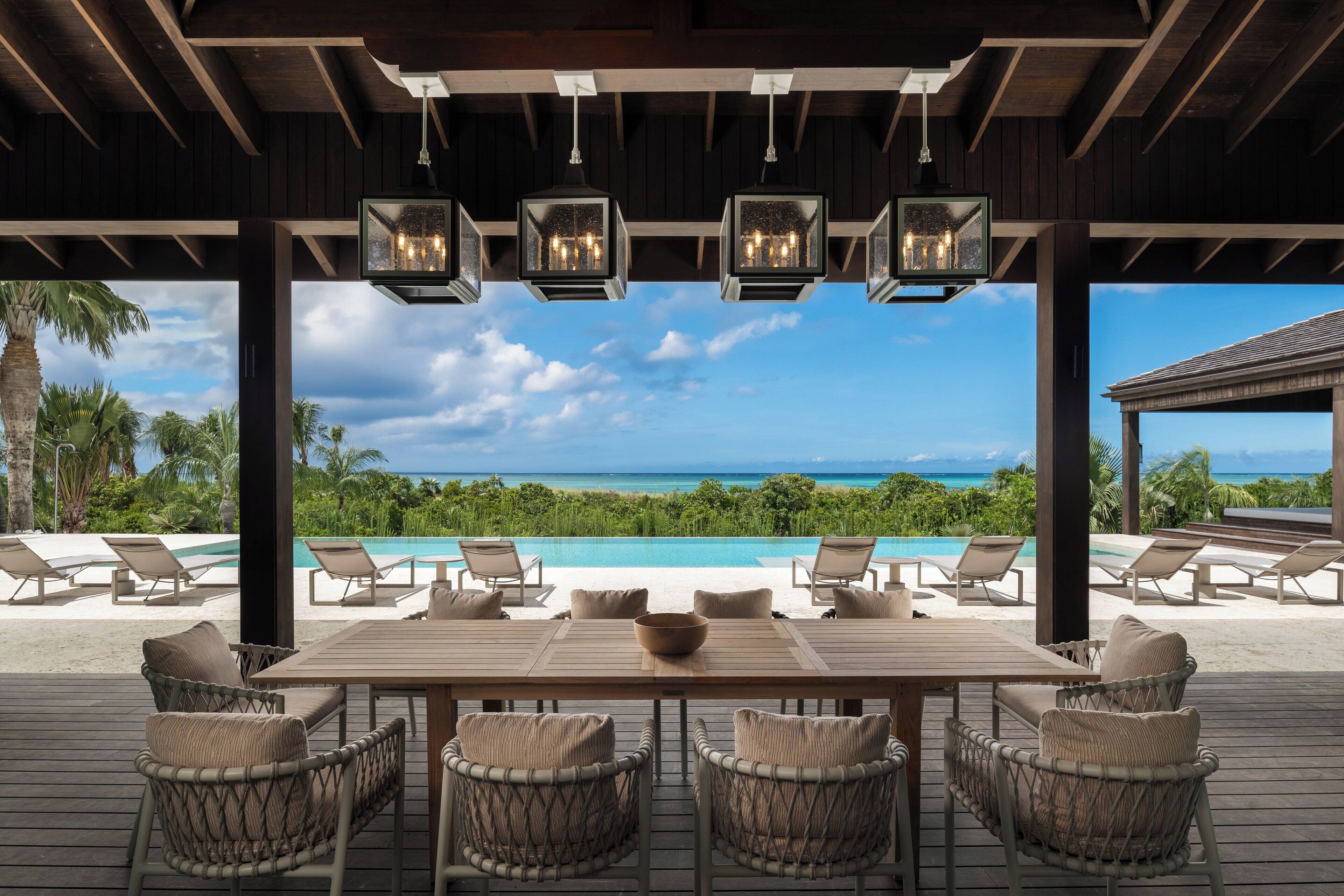 A wooden deck with a table and chairs, overlooking a pool and ocean view.