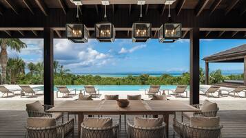 A wooden deck with a table and chairs, overlooking a pool and ocean view.