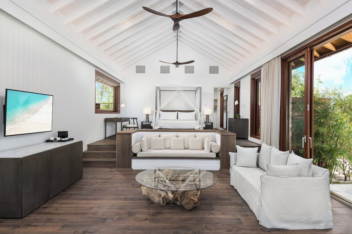 A spacious living area with a modern design, featuring a large sofa, a glass coffee table, and a ceiling fan.