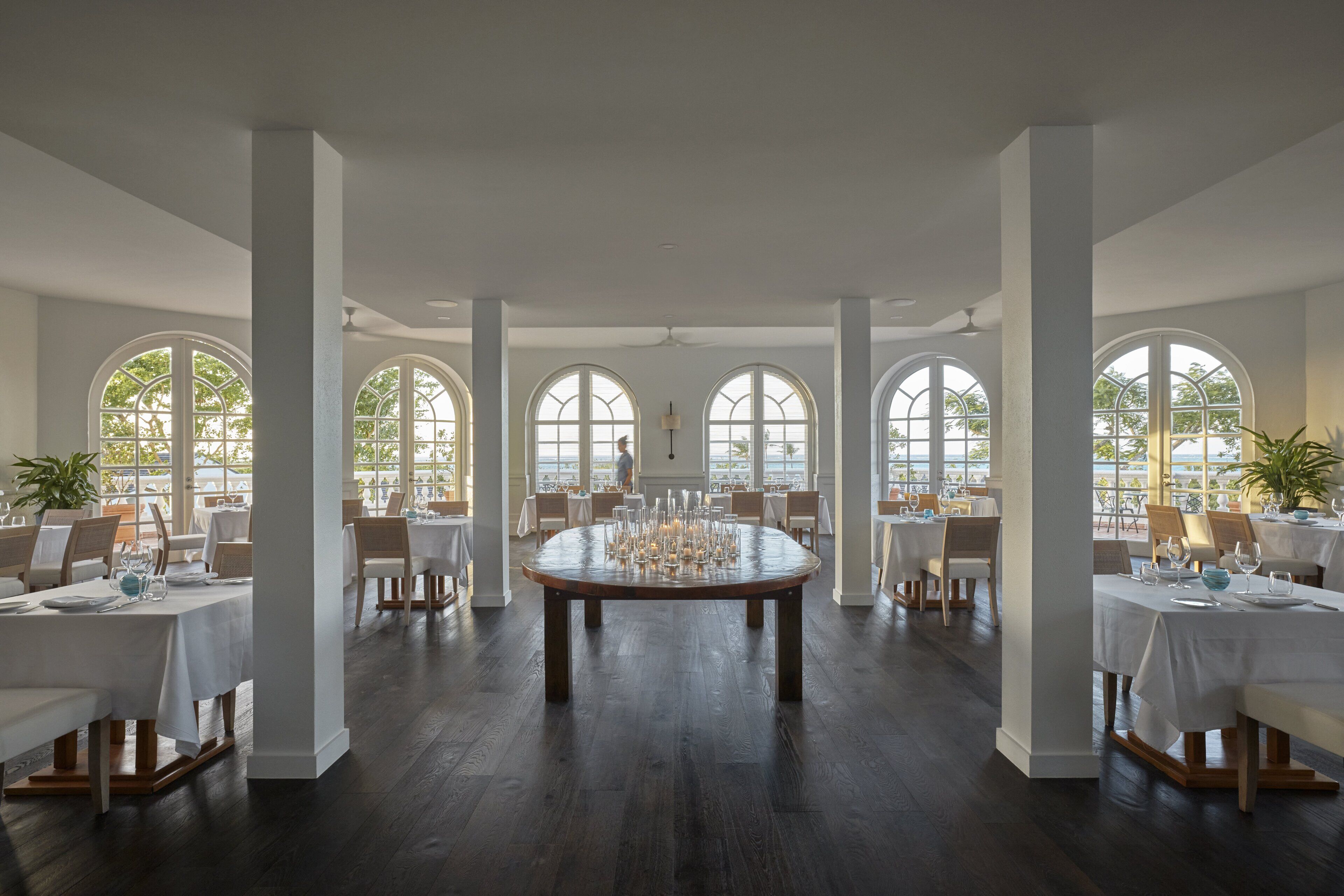 Un comedor amplio con una mesa redonda dispuesta para una comida, ventanas arqueadas grandes y vistas al exterior.