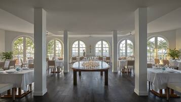 Un comedor amplio con una mesa redonda dispuesta para una comida, ventanas arqueadas grandes y vistas al exterior.