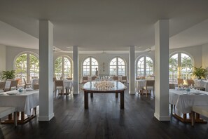 A spacious dining area with a round table set for a meal, large arched windows, and a view of the outdoors.
