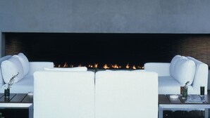 A modern outdoor seating area with a fireplace, white sofas, and a small table with drinks. - Habita, Mexico City, a Member of Design Hotels (Mexico City)
