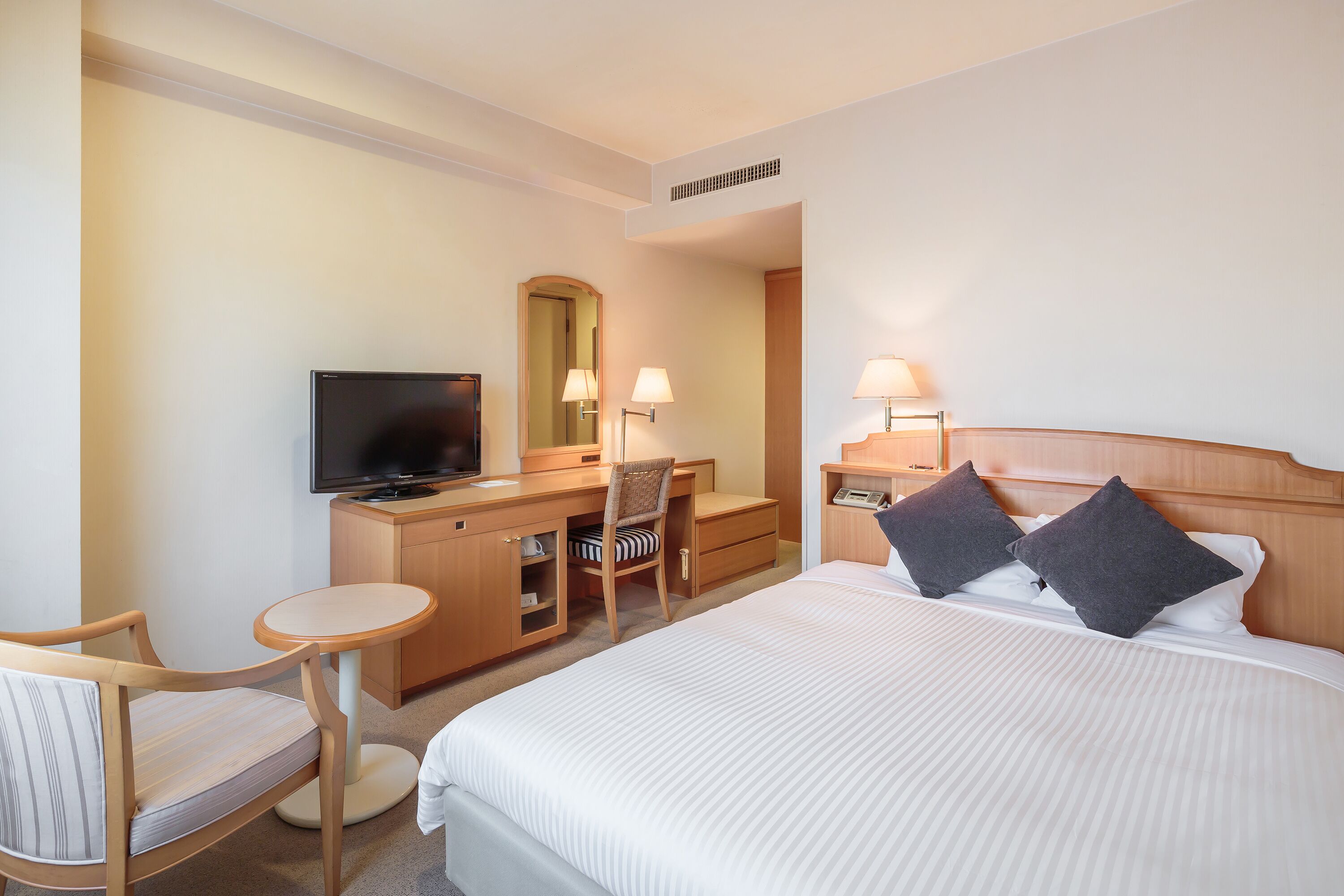 A hotel room with a bed, a desk with a chair, a television, and two bedside lamps.