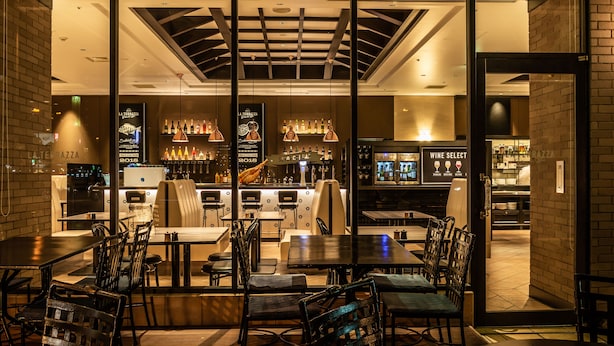 An indoor restaurant with tables and chairs, a bar area with bottles, and a menu board.