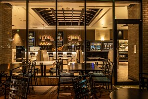 Un restaurante con mesas y sillas, una zona de bar con botellas y un panel con la carta.