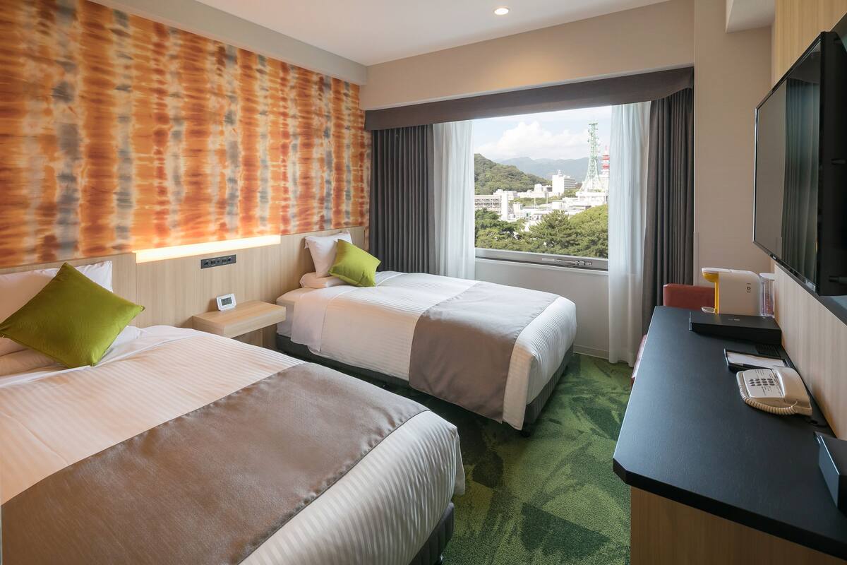 Une chambre d’hôtel avec deux lits, un bureau avec un téléphone et une télévision.