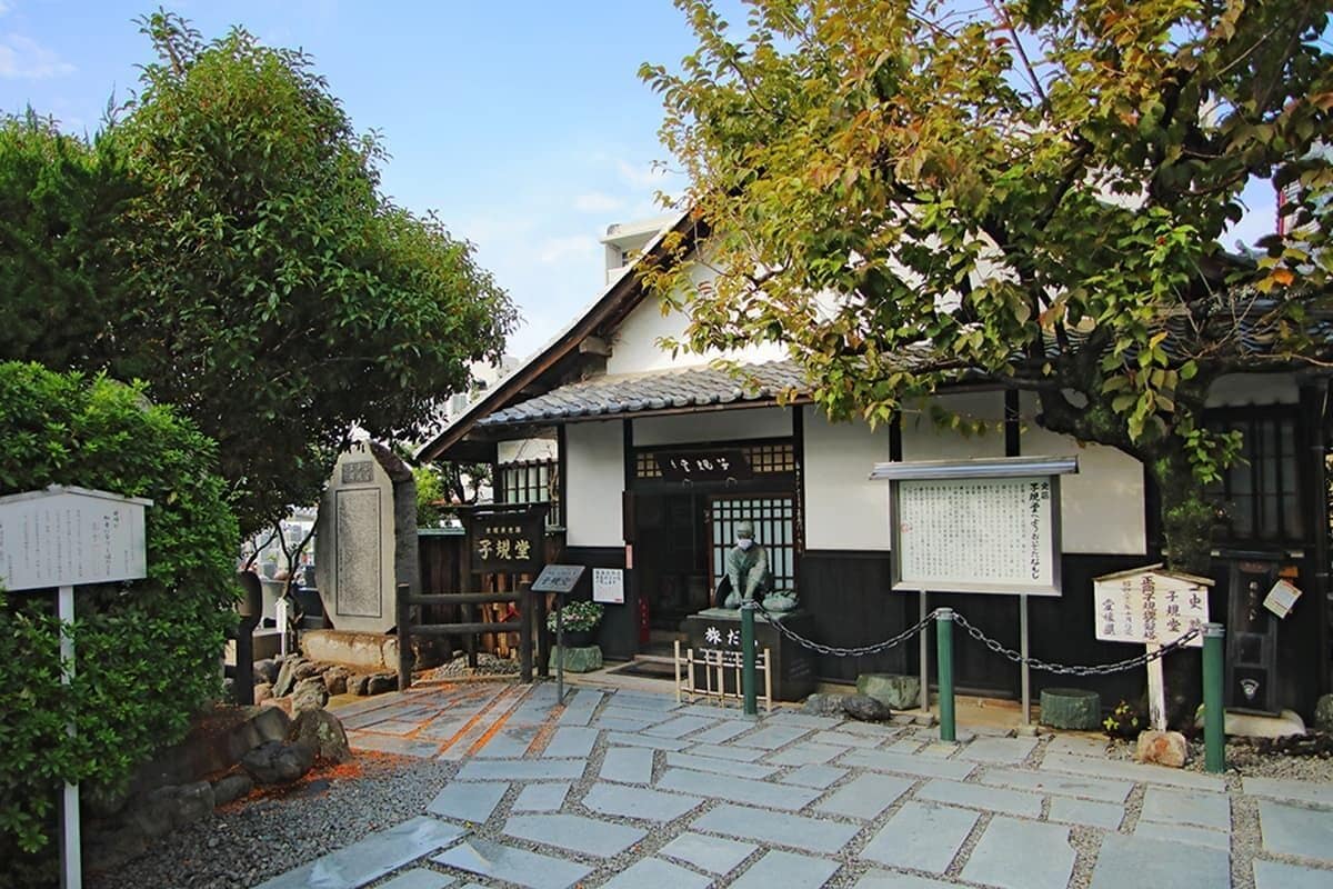 Un edificio japonés tradicional con tejado de tejas, vigas de madera y un sendero de piedra que conduce a la entrada.