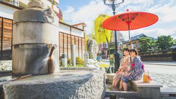 A stone fountain with a traditional Japanese design, a red umbrella, and a stone bench with people sitting.