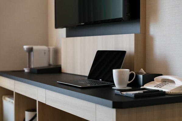 Un mostrador de hotel con una computadora portátil, un teléfono, una taza y una caja.