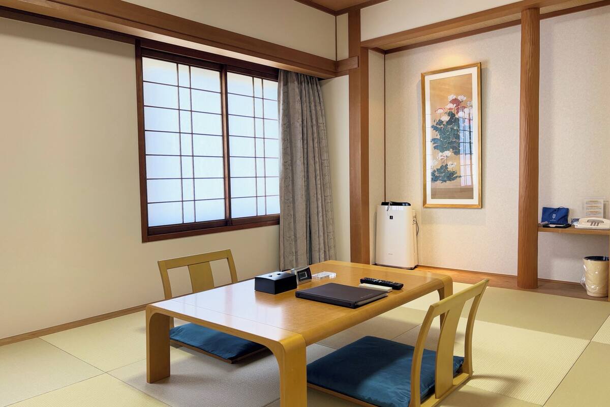 Une pièce de style japonais traditionnel, avec un sol recouvert de tatamis, une petite table en bois et une fenêtre à panneaux coulissants de type shoji.