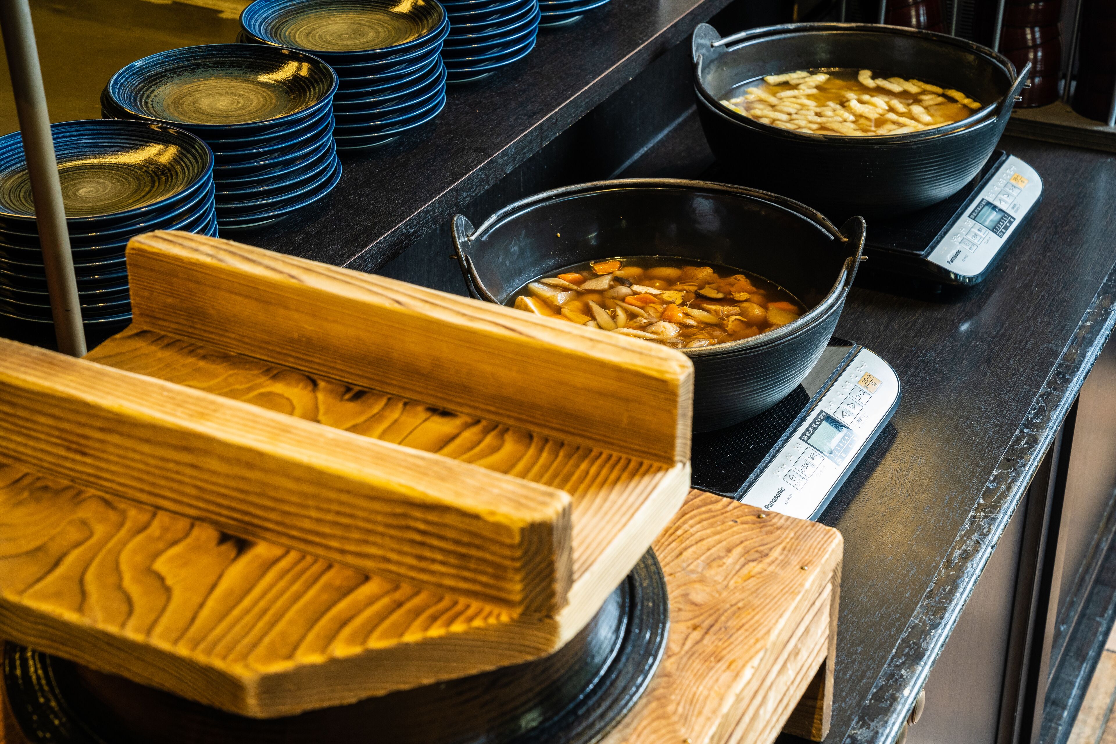A kitchen with stacked blue plates, a bowl of soup, and a weighing scale.