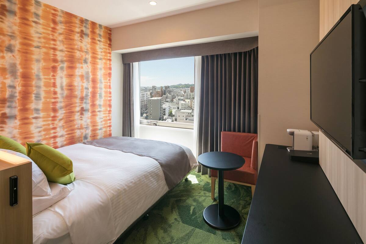 Une chambre d’hôtel avec un lit, une petite table, une télévision et une vue sur la ville.