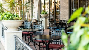 An outdoor seating area with tables and chairs, surrounded by potted plants and a brick wall.