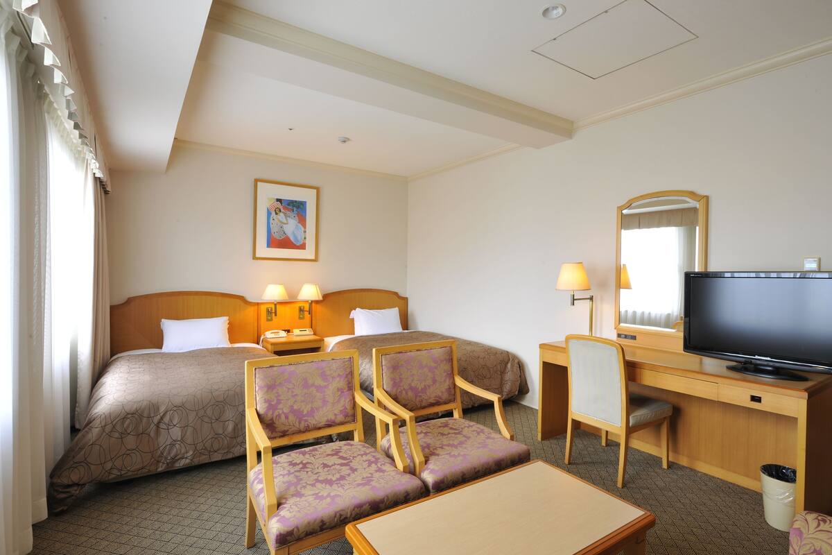 Une chambre d’hôtel comprenant un lit, deux fauteuils, un bureau avec une télévision et une lampe.