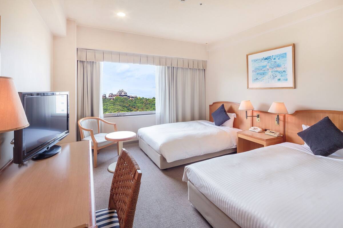 Une chambre d’hôtel avec deux lits, une télévision, un bureau et une chaise.