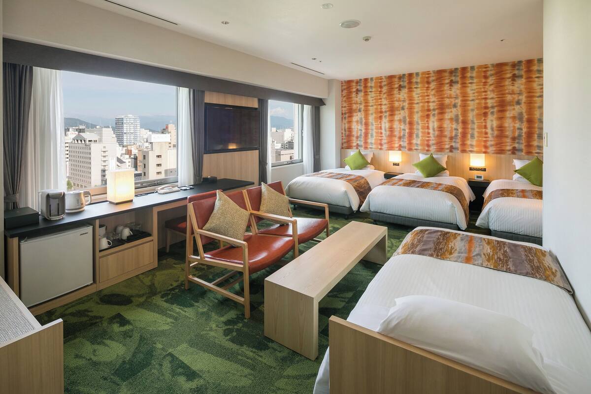 Une chambre d’hôtel avec vue sur la ville, un bureau, une chaise, deux lits et une moquette verte.