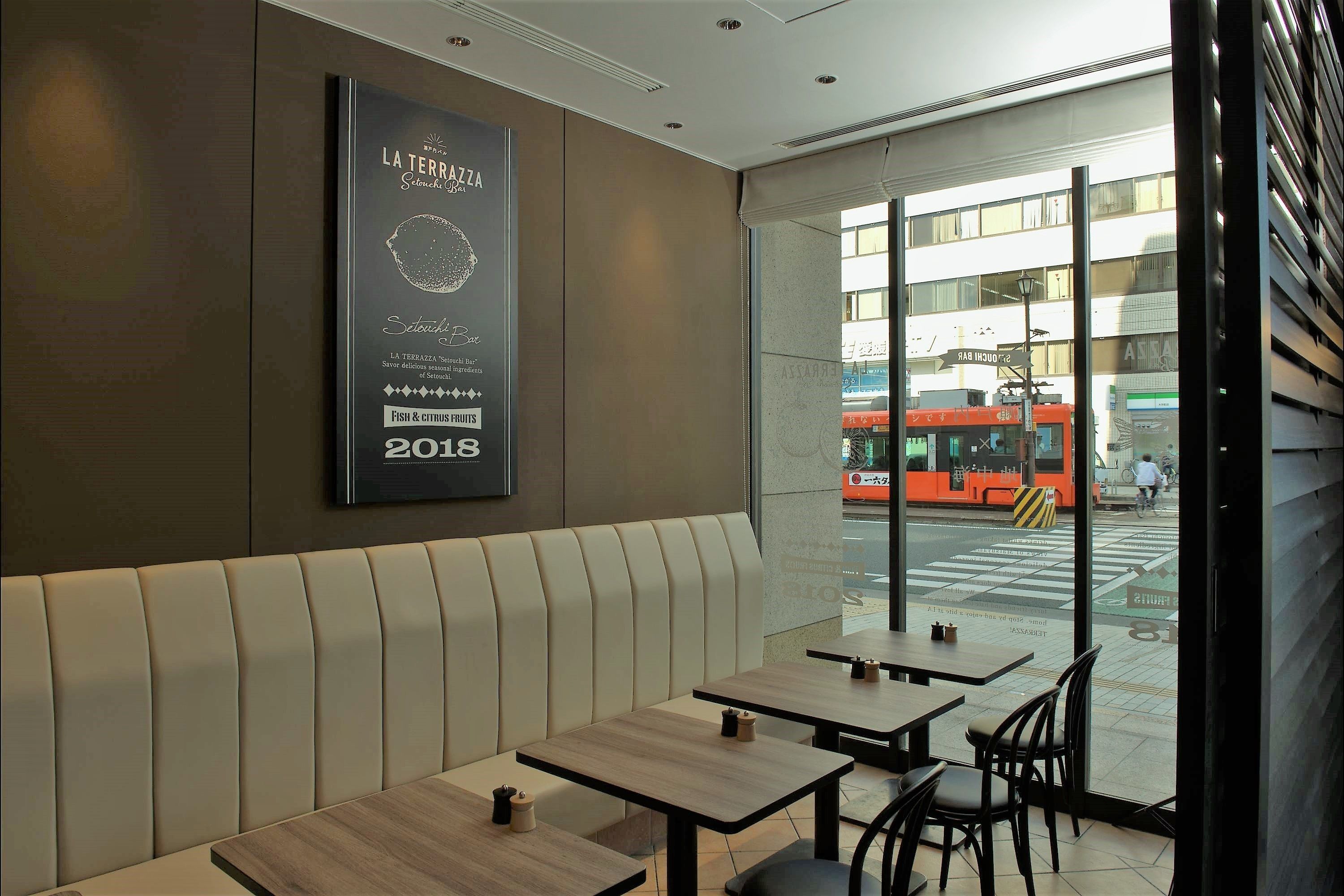 A modern restaurant interior with a large poster on the wall, several wooden tables, and a view of the street outside.