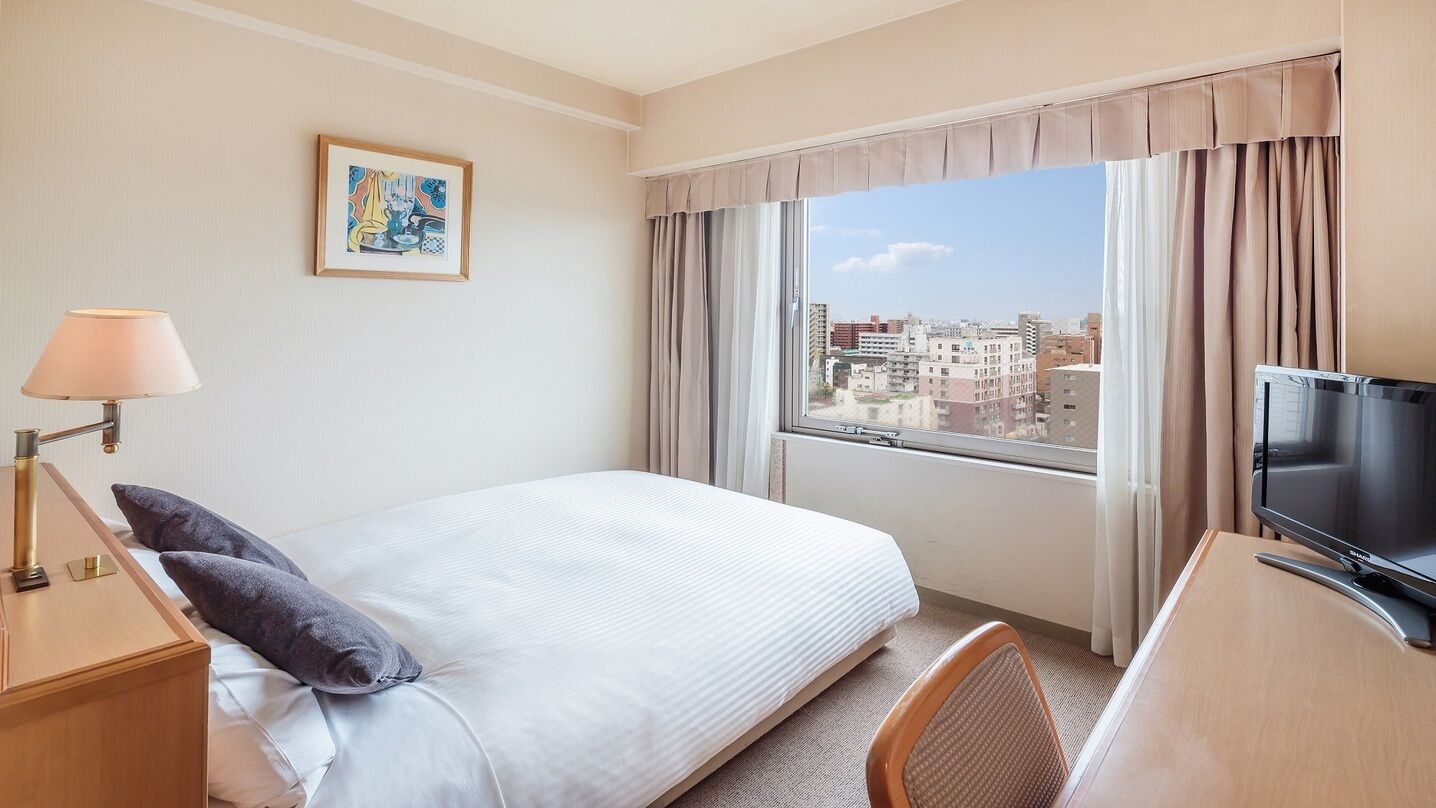 A hotel room with a bed, a desk with a television, a window with curtains, and a painting on the wall.