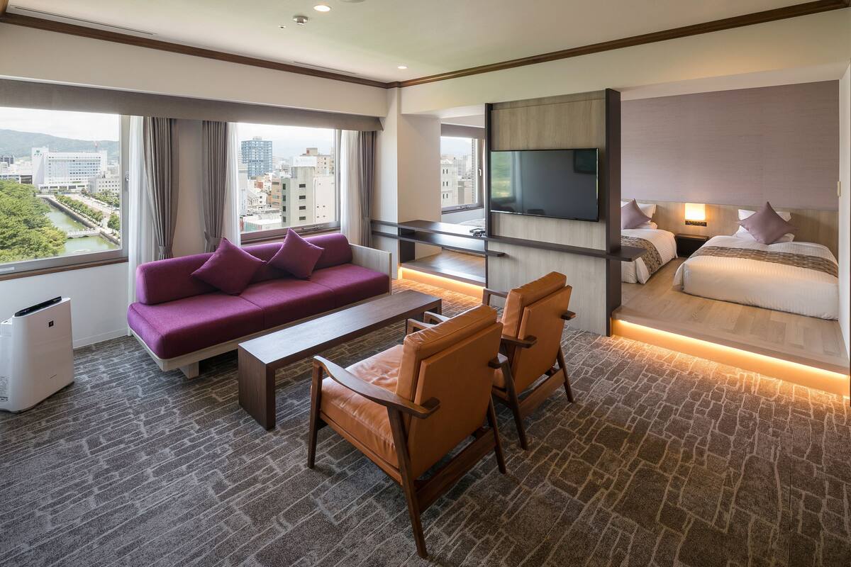 Une chambre d’hôtel avec un canapé, deux fauteuils, un lit, une télévision et une vue sur la ville.