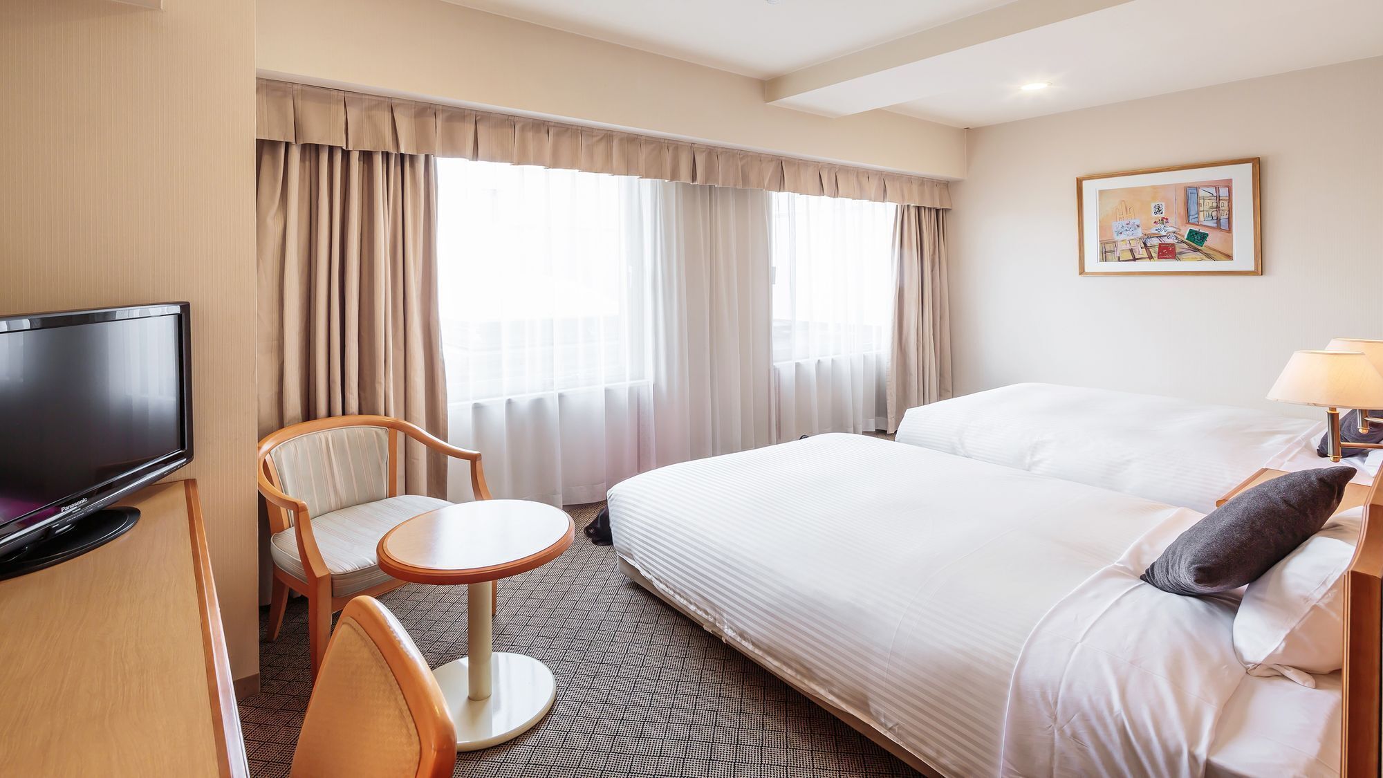 A hotel room with a bed, a TV, a chair, a small table, and curtains.