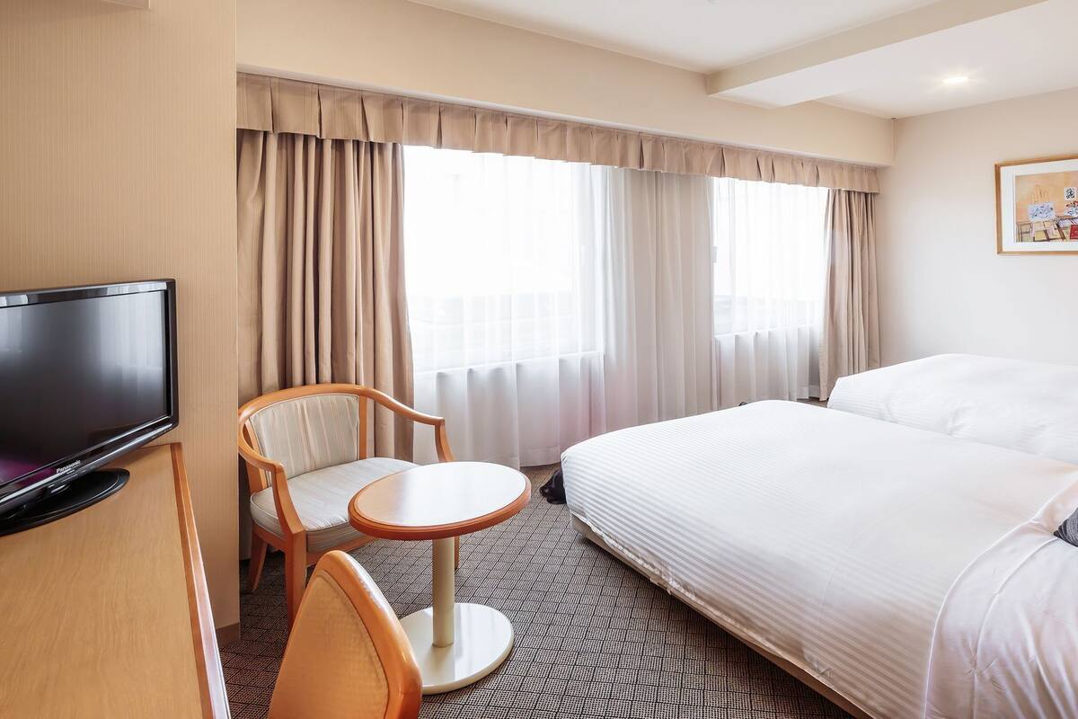 Une chambre d’hôtel avec un lit, une télévision, une chaise, une petite table et des rideaux.