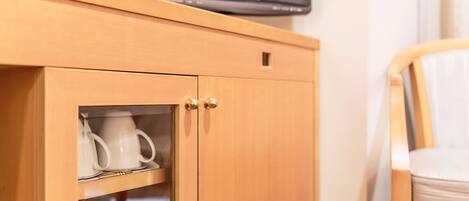 Un mueble de madera con un televisor encima, una puerta de cristal que contiene una taza blanca y un objeto pequeño en su interior, y una silla de madera con cojín.