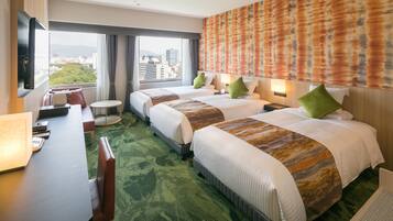 A hotel room with two beds, a desk, and a view of the city.