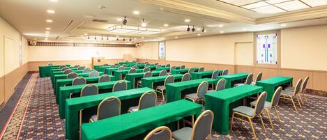 A conference room with rows of tables and chairs, a patterned carpet, and a ceiling with recessed lighting.