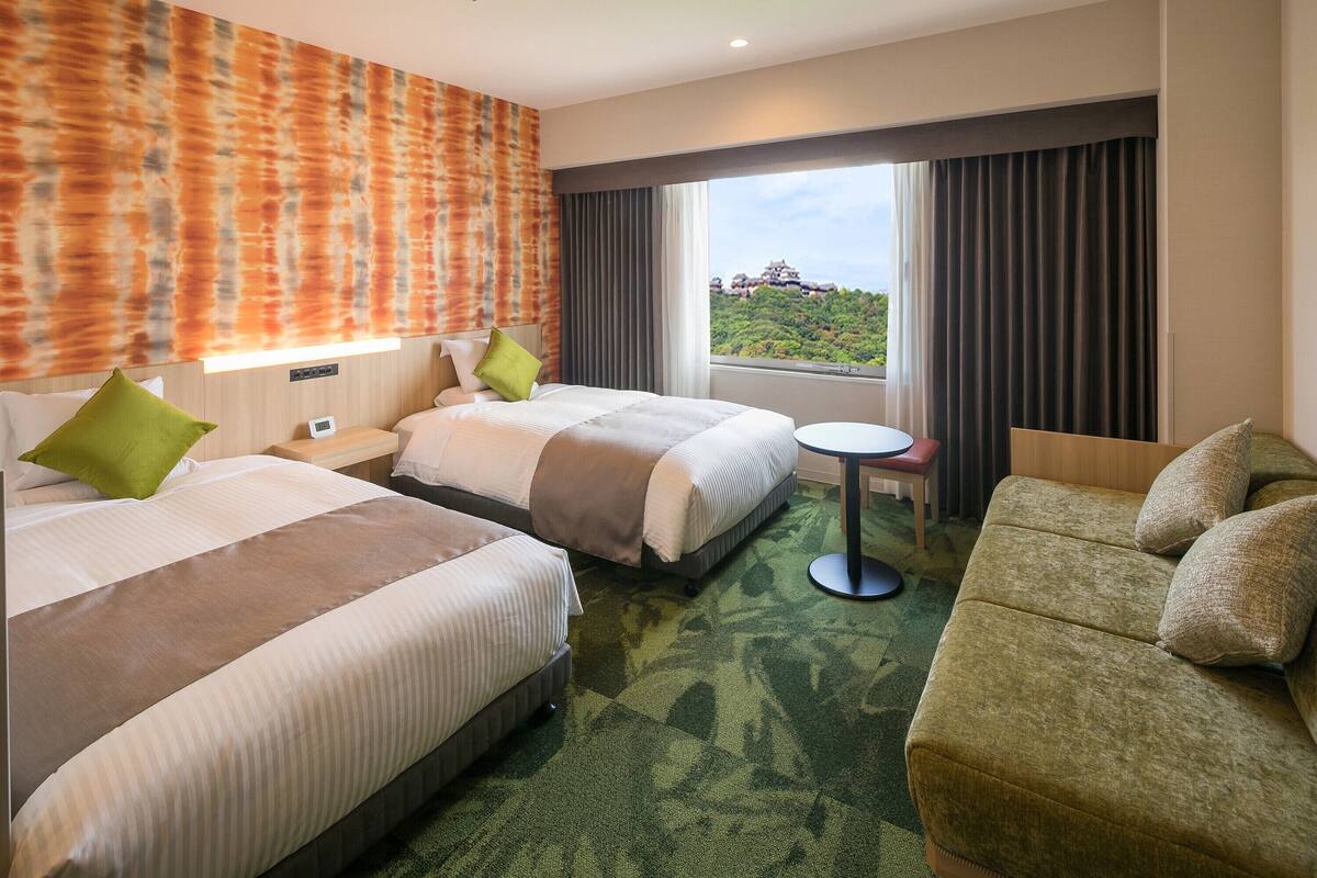 Une chambre d’hôtel avec deux lits, un canapé, une petite table et une vue sur un paysage montagneux.