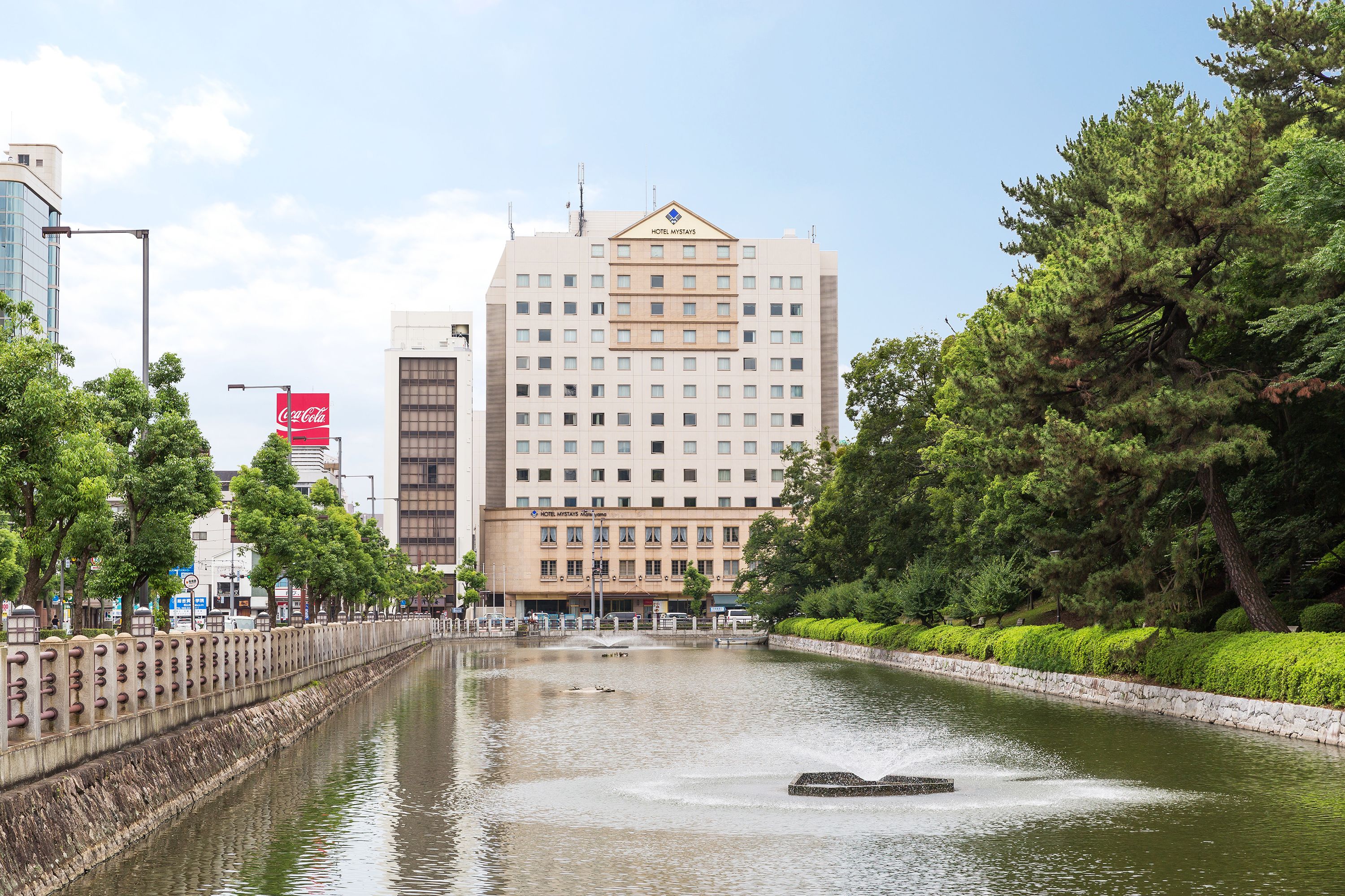 A hotel with a water canal in front, surrounded by greenery and modern buildings.