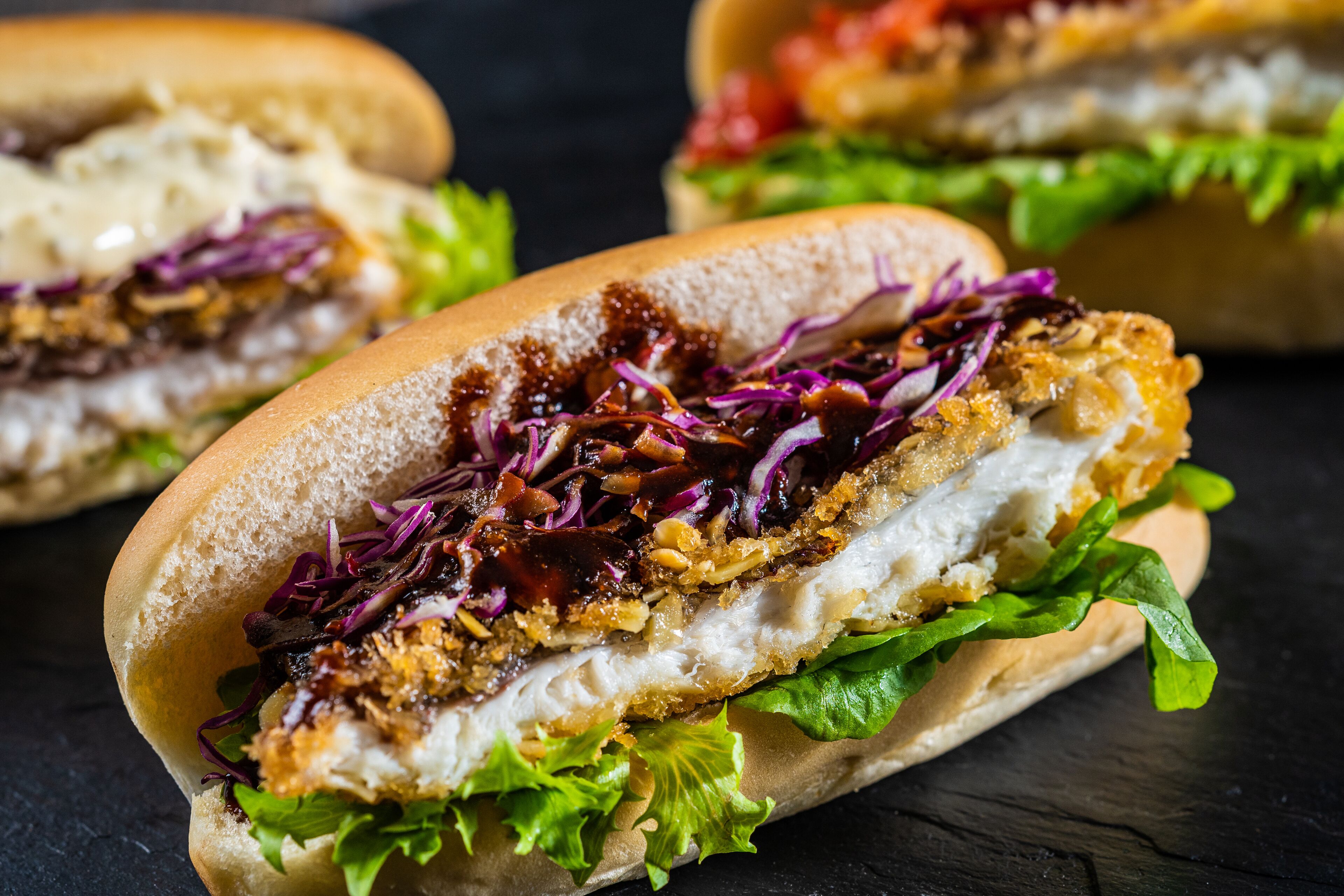 A sandwich with lettuce, red cabbage, and a crispy breaded chicken breast.