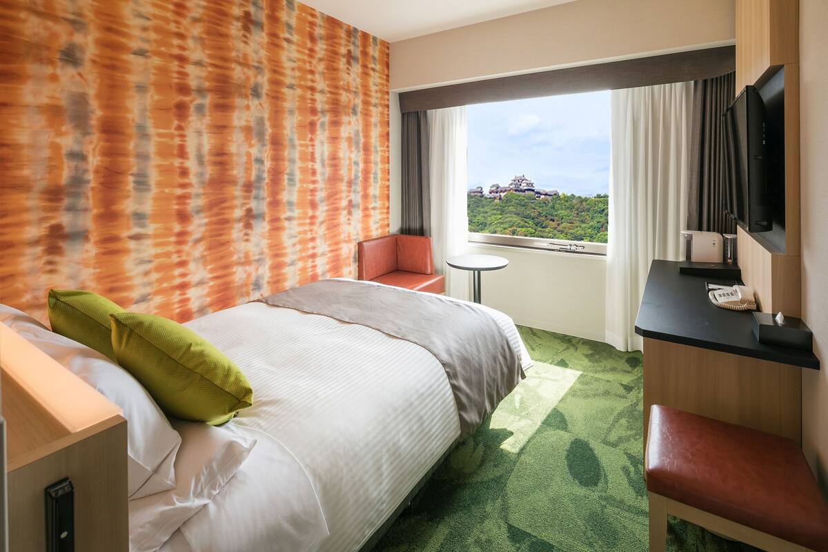 Une chambre d’hôtel dotée d’un grand lit, d’un bureau avec un téléviseur à écran plat, d’une petite table et offrant une vue sur un paysage montagneux.