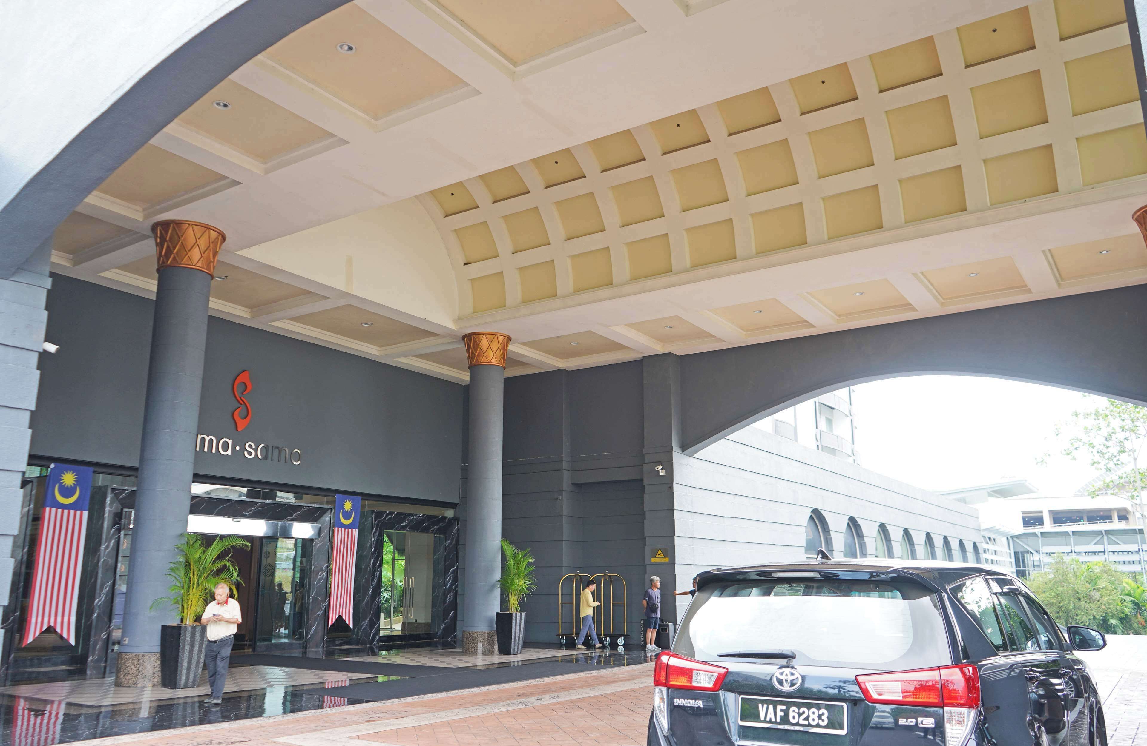 A modern hotel entrance with a large overhang, prominent pillars, and a sign reading 'ma-sama.'